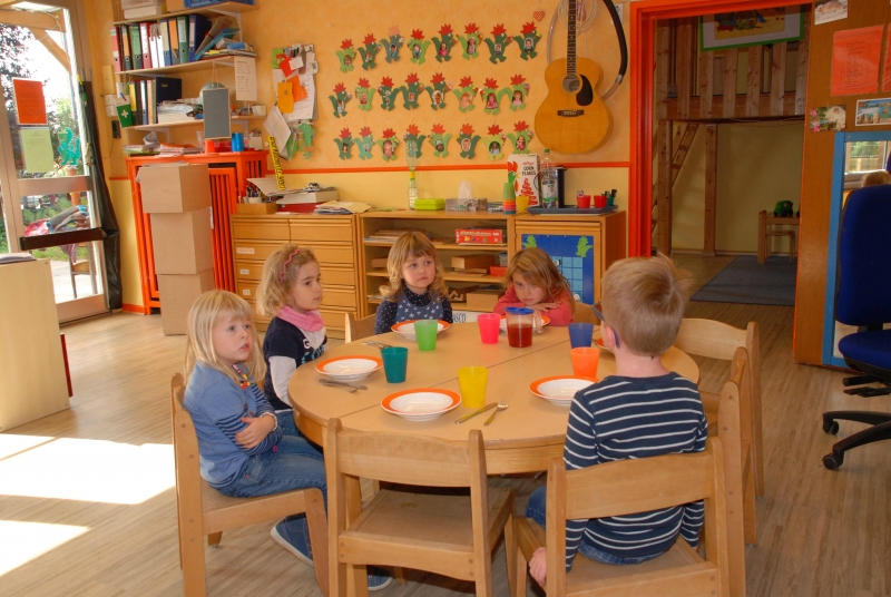 Fünf Kinder sitzen am Tisch und warten mit leeren Tellern auf das Essen.