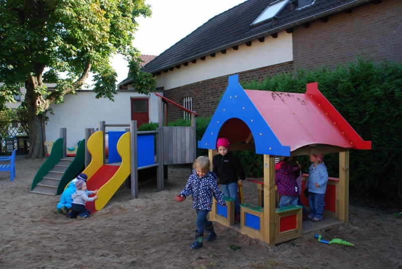 Kinder Spielen im Außengelände im Holzhaus und an der Rutsche.